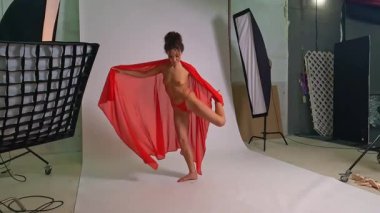 Canlı bir dans stüdyosunda, güzel bir kadın zarif bir şekilde üstsüz poz verir, hareketlerini arttırmak için kırmızı bir kumaş kullanır. Ayarda, kişisel oturum sırasında sanatının ve biçiminin vurgulandığı profesyonel ışıklandırma yer alıyor.