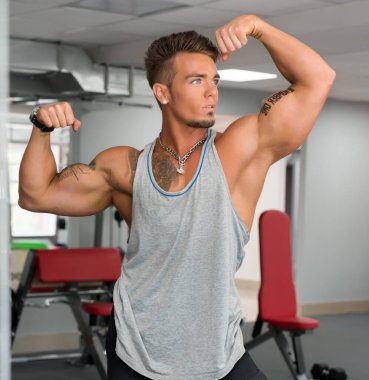 Spor salonunda. Onun pazı gösterilen poz yakışıklı erkek atlet