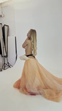 Göz kamaştırıcı bir kadın zarif pozlar sergiliyor. İyi aydınlatılmış bir stüdyoda, dalgalı turuncu bir elbise ve ışıldayan bir güzellik giyiyor..