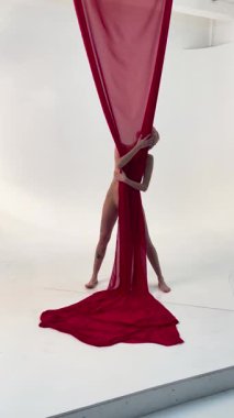 Kendine güvenen bir kadın, sahne arkasında yaratıcı bir atmosferde kırmızı kumaşla kaplıyken güzelliğini sergiler..