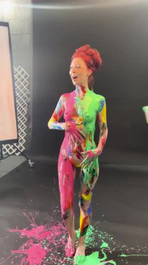 Bir kadın kuliste kendine güvenerek poz veriyor, renkli vücut sanatı sergiliyor, neşeli boya sıçramaları ve canlı tasarımlarla..