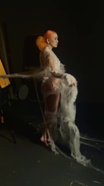 Kırmızılı çarpıcı bir kadın zarif bir şekilde büyük bir ağa yakalanıyor ve karanlık bir ortama karşı büyüleyici bir görüntü yaratıyor..