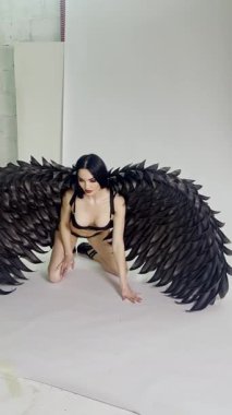 Stüdyoda, bir kadın güzelliğini arttıran çarpıcı kanatları sergilerken zarifçe diz çöker..