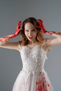 Kana bulanmış gelinlik giymiş bir kadın dramatik bir şekilde poz verir, elleri kırmızı ve ifadesi vahşidir..