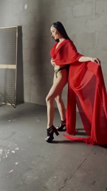 Bir kadın zarif bir şekilde kırmızı bir elbiseyle poz verir, minimalist bir stüdyo ortamında güzelliği yakalar..