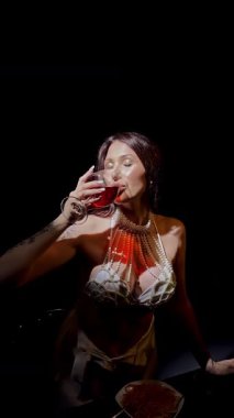 Şık bir kadın, karanlık bir stüdyoda spagetti ve şaraptan zevk alır. Zarafet ve yemek zevki yayar..