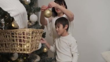 Mutlu ebeveynler ve küçük oğlu evde birlikte Noel ağacına top asıyorlar.