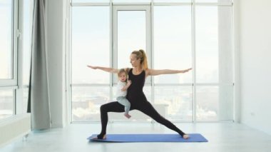 Güzel sarışın kız yoga yapıyor. Küçük tatlı oğlunu kucağında tutuyor. Stüdyoda egzersiz yaparken bacağının üstünde oturuyor.