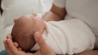 Sevimli yeni doğmuş bebek babasının bacaklarının üzerinde uyuyor ve baba sallanan çocuk. Bebek bebek battaniyeyle kundaklanmış ve ailesi onu önemsiyor.