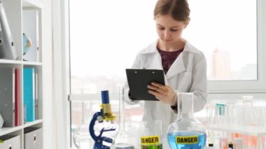 Liseli kız kimya dersinde tüpler ve tehlikeli uyarılarla notlar alıyor. Laboratuvarda okuyan kız öğrenci.