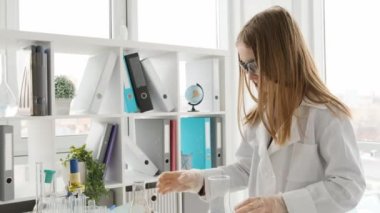 Korunma gözlüğü takan liseli kız kimya dersinde mavi ve turuncu sıvılı şişelere bakıyordu. Laboratuvarda ekipmanla çalışan bir kız öğrenci.