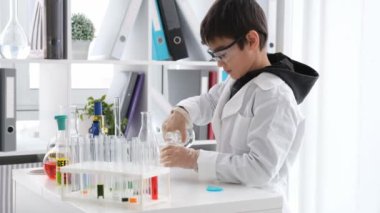 Kimya dersindeki öğrenci sınıfta bardağı sıvı tüpler ve test için ekipmanlarla dolduruyor. Öğrenci çocuk laboratuarda çalışıyor.