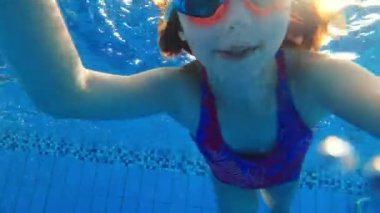 Gözlüklü şirin bir kız havuzda suya dalıp yüzüyor. Çocuk suda selfie çekiyor..