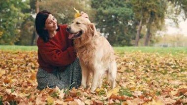 Genç bir kadın sonbahar parkında altın renkli köpekle eğleniyor..