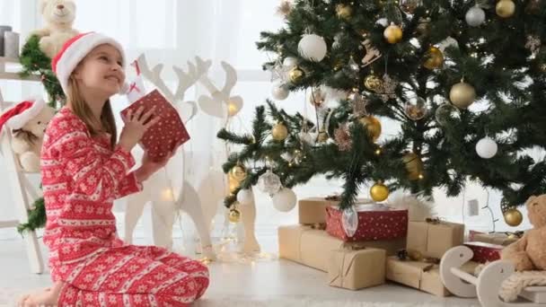 Όμορφο Κορίτσι Δώρα Κοντά Στο Χριστουγεννιάτικο Δέντρο Φορώντας Κόκκινο Καπέλο — Αρχείο Βίντεο