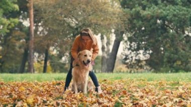 Mutlu küçük kız sonbahar parkında eğleniyor ve altın renkli köpekle oynuyor..