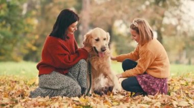 Anne ve kızı sonbahar parkında altın renkli köpekle eğleniyorlar. Mutlu aile eğitimleri ve dışarıda köpeklerle oynamalar..