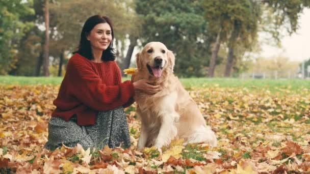 秋の公園で黄金のレトリバー犬と楽しい時間を過ごしている母親と娘 犬と屋外で遊ぶ幸せな家族 — ストック動画