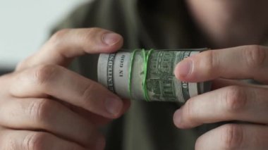 Yüz dolarlık banknotları elinde tutan adam lastik bantla sarıp, manzarayı kapatıyor.