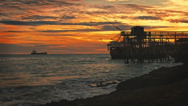 日没時に釣り小屋やネットとフランスのサンパレのロッキー海沿岸のビーチ 魚の捕獲と夕方のオレンジの空のための収縮と海の海岸 — ストック動画