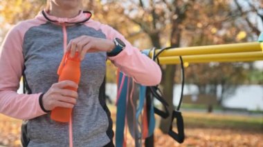 Sonbahar parkında spor yaptıktan sonra elinde eko-su şişesi tutan fitness kızı. Spor kadını antrenman sırasında vücudunu sulandırır.