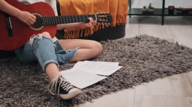 Genç kız evde yerde oturup gitar çalışıyor. Müzik aleti çalma dersi