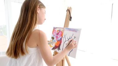 Little girl painting on easel in art studio. Schoolgirl learn to paint colourful abstract painting.