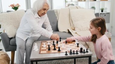 Granddaughter shows to grandmother strategy of game during playing chess