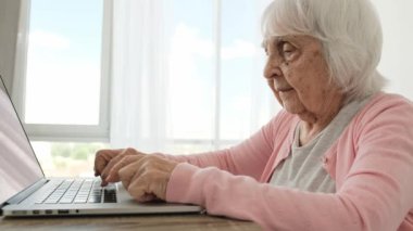 Dizüstü bilgisayarda yazı yazan son sınıf öğrencisi bir kadın. Evde yavaş yavaş. Yaşlı kadın defter tuşlarına basıyor ve ekrana bakıyor