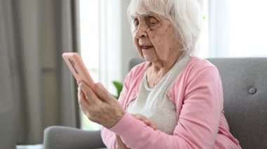 Senior woman using smartphone for video call and talking. Elderly female person with cell phone communicating at home