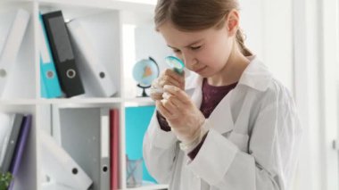School girl looking at test results through zoom glass in chemistry class. Female pupil studying in lab