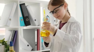 School girl wearing glasses with bottle filled with orange liquid in chemistry class. Female pupil kid studying in lab