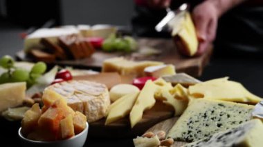 Girl slicing cheese maasdam. Mix cheese with grapes and nuts, cheese plate. Wine appetizer on black background.