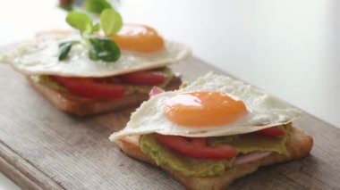 Person hands preparing bread with avocado, tomatoes and eggs for breakfast and putting greans. Healthy rustic nutrition food with toasts and guacamole