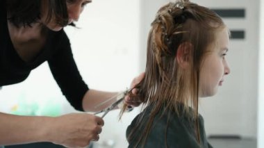 Hairdresser makes haircut for preteen girl with scissor. Female child in beauty salon during hairstyling