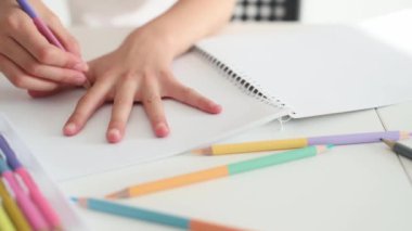 Child outlines her hand with crayon from coloful palette and drawing on white paper. Person kid painting with pencils