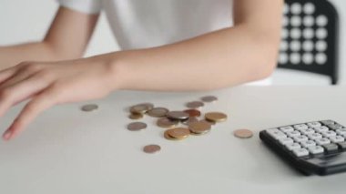 Child hands take out coins from wallet on table and going counting with calculator. Kid with money at home