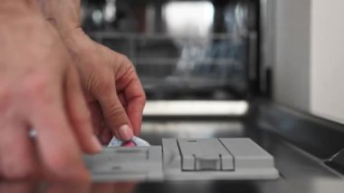 Girl put dishwasher pill and close the door of a dishwasher at kitchen. Woman and washer machine at home