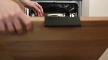 Girl hand open dishwasher door with clean dishes inside at kitchen. Woman and utencil in washer machine