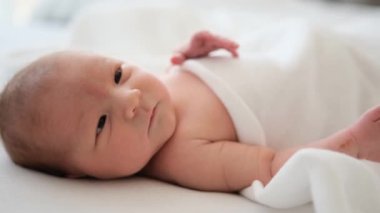 Portrait of adorable newborn baby lying on the bed at home with daylight, moving hands and looking around. Innocent beautiful infant child resting in bedroom
