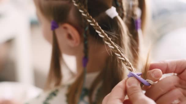 サロンで美しい髪を持つ子供の女の子のためのバーバー編組ピグテールヘアスタイル 流行のヘアスタイルの閉鎖中の美容師の手 — ストック動画
