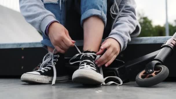 乗る前にスクーターネクタイの靴ひもを持つ14人の女の子 スニーカーで子供の足を閉じます — ストック動画