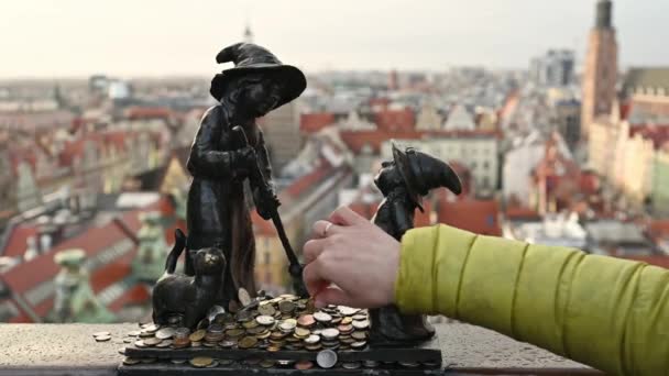 観光客の手は 都市の景色を望むポーランドのヴロツワフで有名なドワーフのノーム彫刻にコインを入れました 欧州連合 の国のお金の伝統と記念碑 — ストック動画