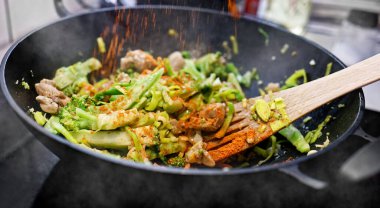 Meat with fresh vegetables cooking in asian wok pan. Red dry ground pepper is sprinkled on the food.