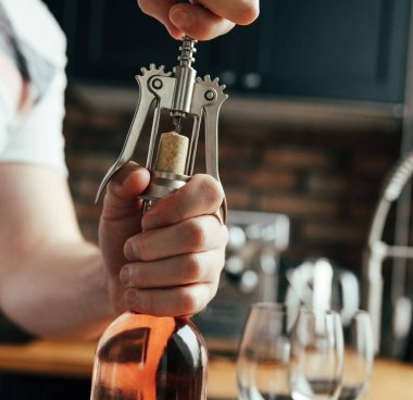 Man opening wine bottle and glasses on table at kitchen