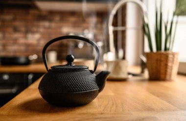Black metal teapot with hot tea at the kitchen. Steam comes from the tea spout. Tea drinking traditions. Girl making a tea.
