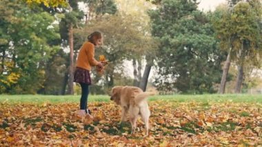 Mutlu küçük kız sonbahar parkında eğleniyor ve altın renkli köpekle oynuyor..