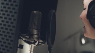 Kayıt stüdyosunda mikrofonla şarkı söyleyen bir kız. Şarkı oluşturma sürecinde genç kadın şarkıcı performansı