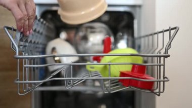 Kirli bulaşıkları bulaşık makinesine ve modern ekipmanların kapalı kapısına kız eli koydu. Çamaşır makinesinde kadın ve kap kacak