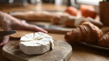 Fransız kahvaltısı için peynirli kruvasanla güneşli mutfakta kruvasan kesen kız elleri. Sağlıklı bir sabah yemeği için lezzetli pastane pastası ve camembert peyniri.